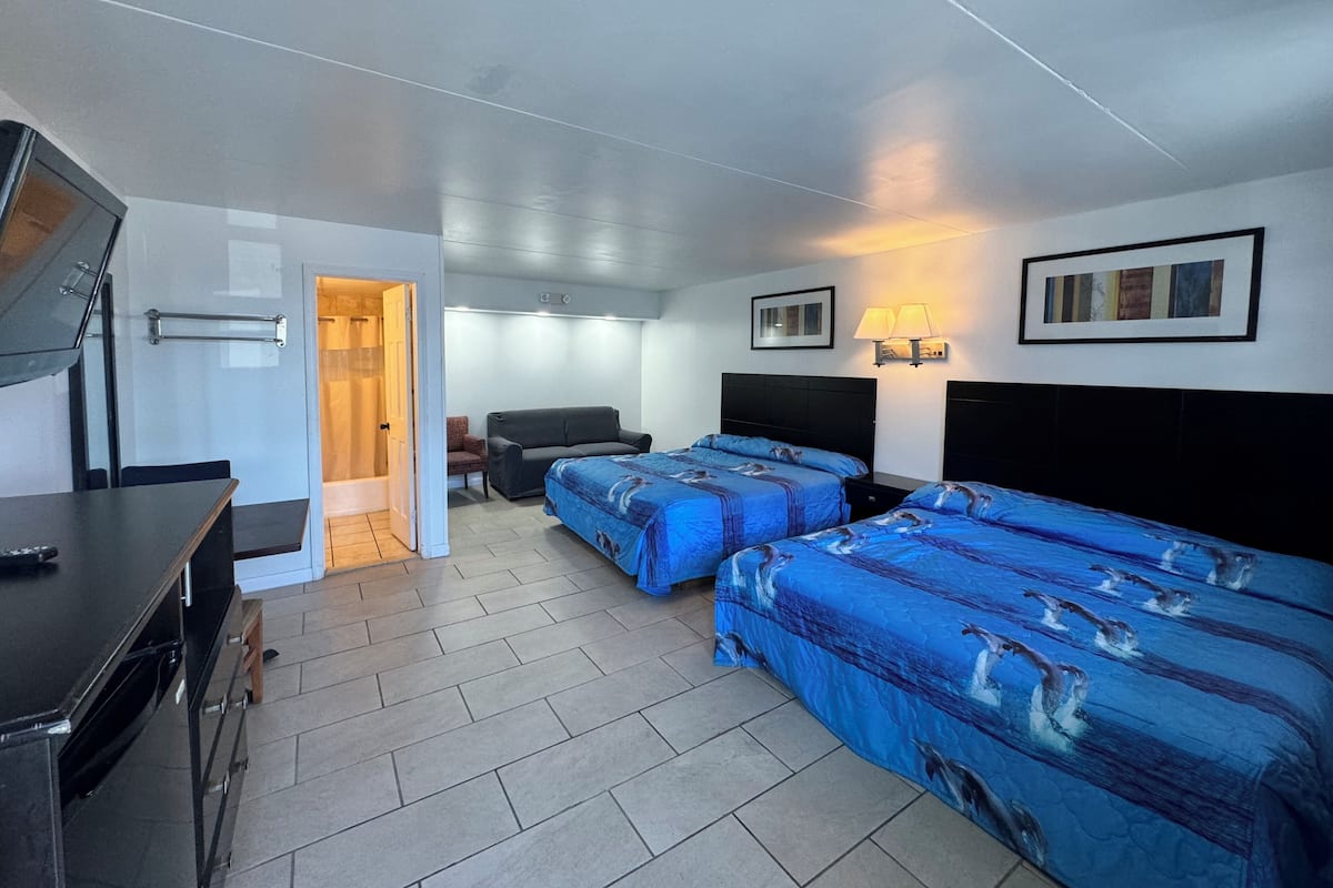 Ein Hotelzimmer mit zwei Betten, einem Schreibtisch, einem Fernseher, einer Dusche und einem Badezimmer.