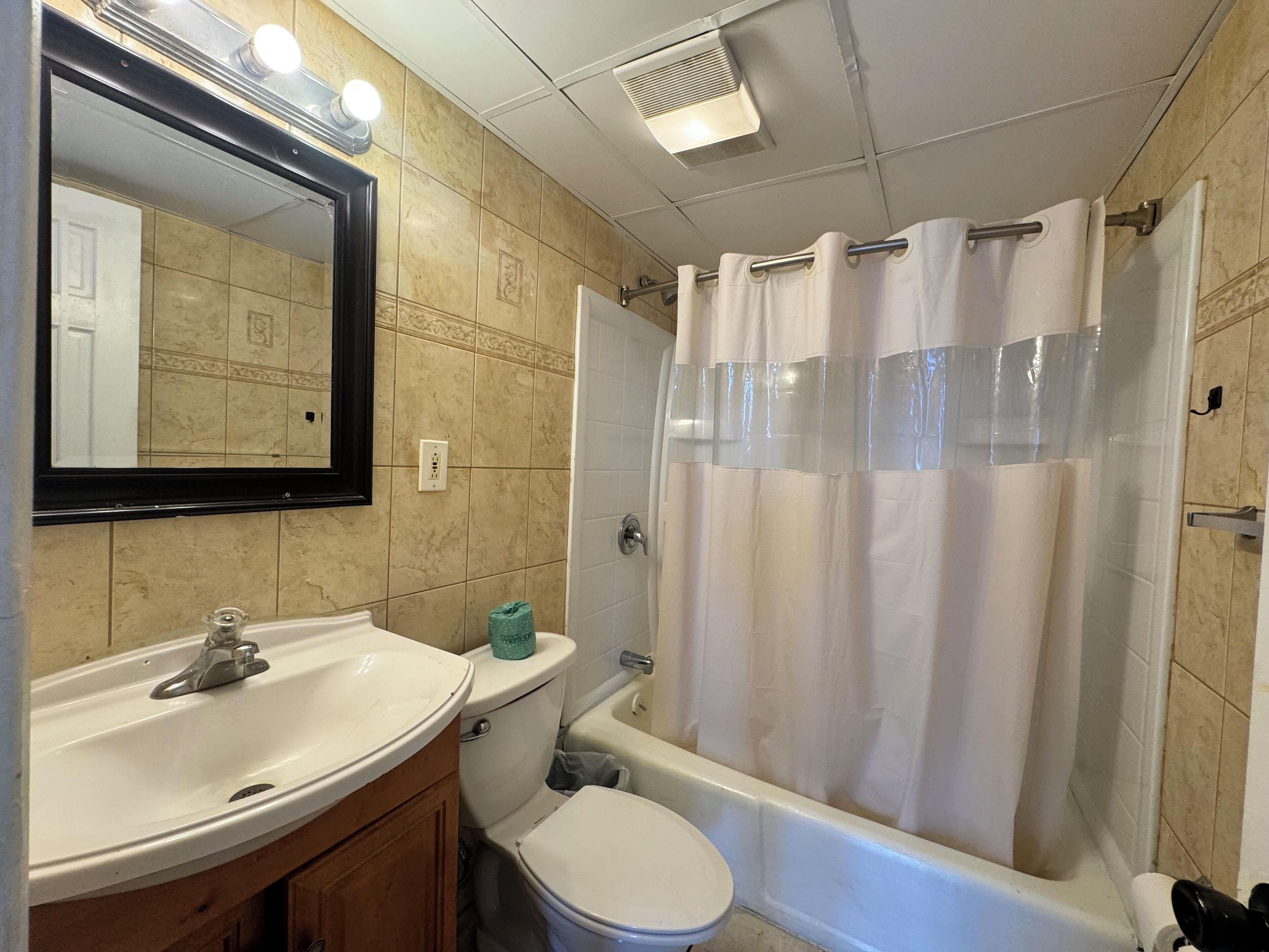 A bathroom with a white sink, toilet, and bathtub. There is a mirror above the sink, and a shower curtain is visible.