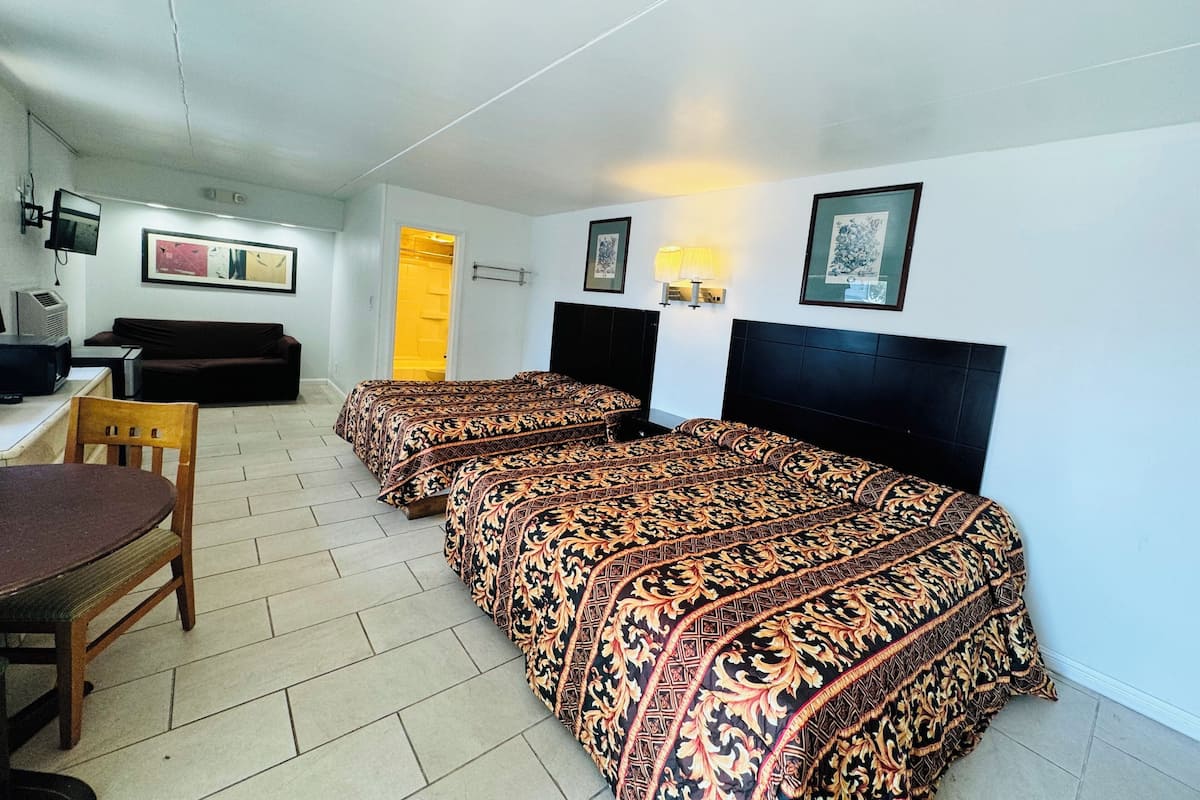 Ein Hotelzimmer mit zwei Betten, einem Schreibtisch, einem Stuhl, einem Fernseher und Bildern an den Wänden.
