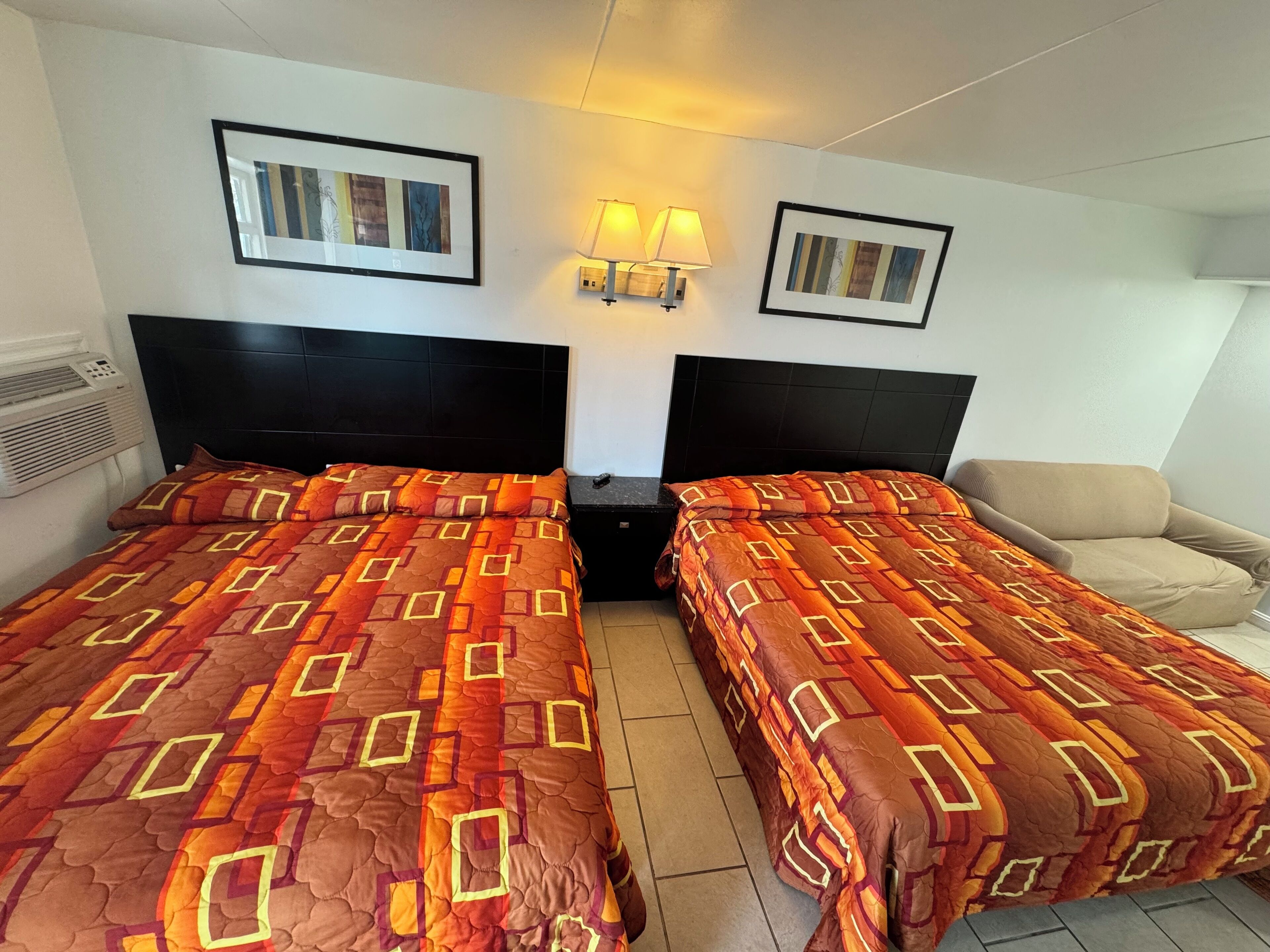 Una habitación de hotel con dos camas, una silla y dos lámparas fijadas a la pared.