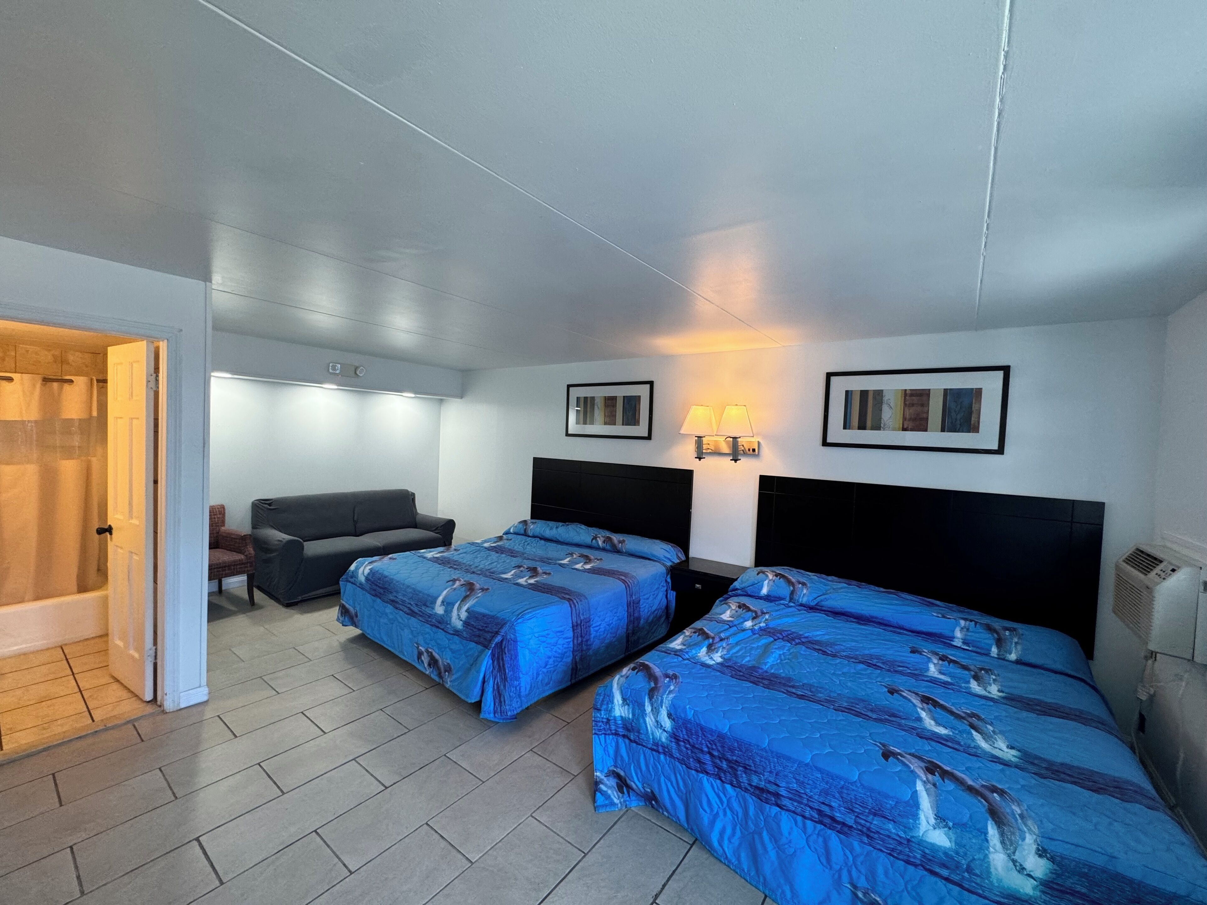 Una habitación de hotel con dos camas, un sofá, ducha y una pequeña mesa.