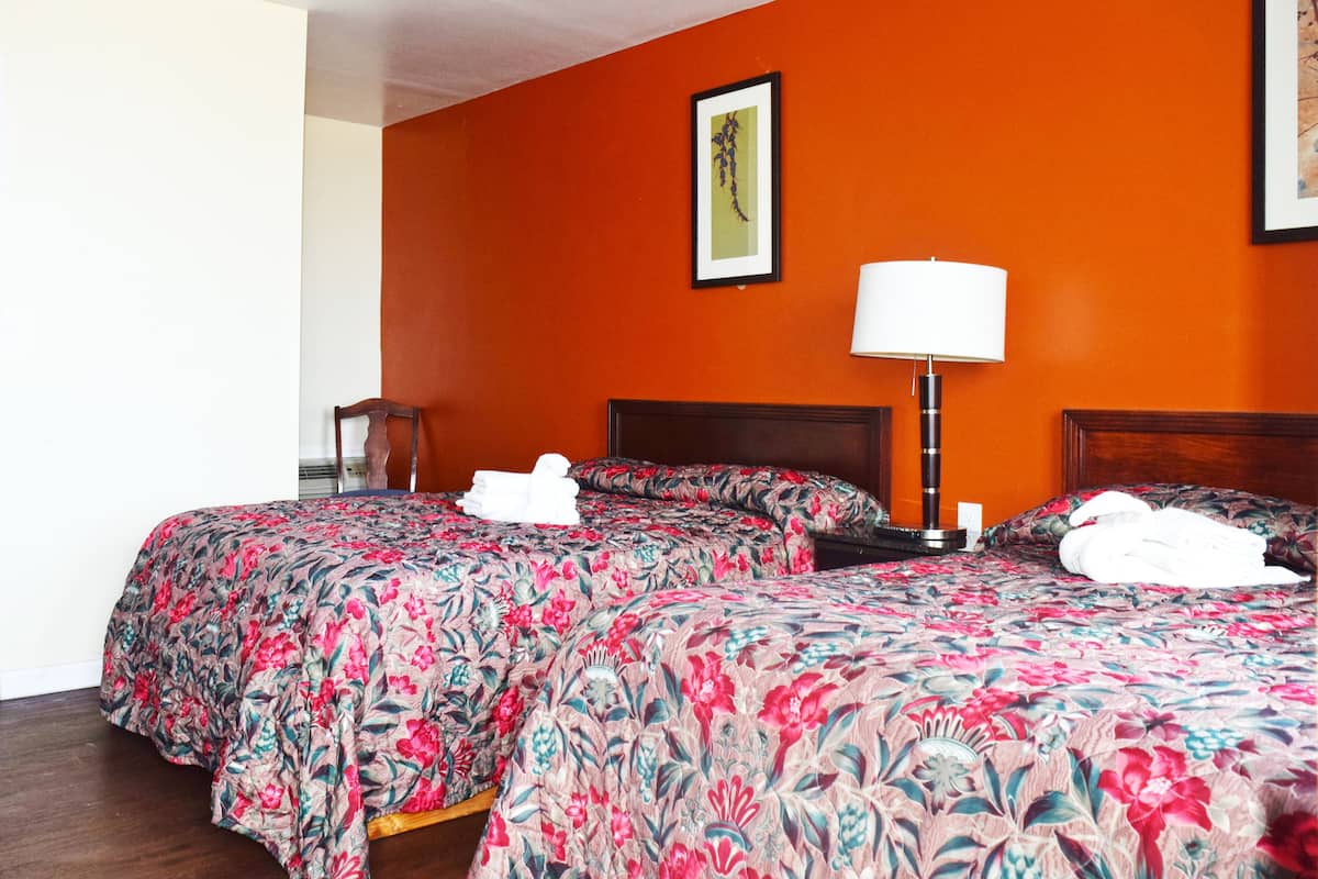 Ein Hotelzimmer mit zwei Betten, einem Nachttisch, einer Lampe und einem gerahmten Bild an der Wand.