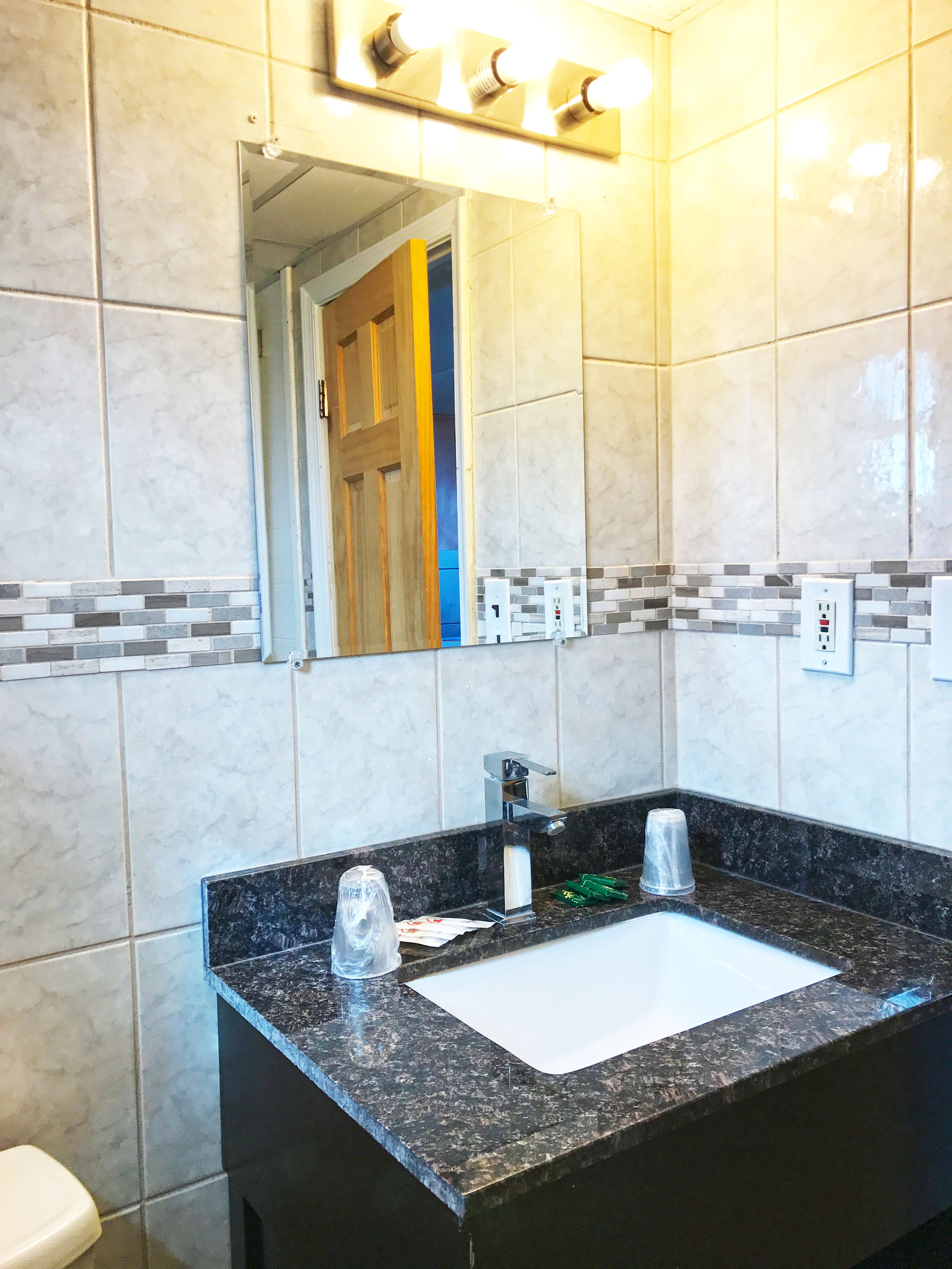 A bathroom with a marble-tiled wall, a sink with a black countertop, and a mirror above the sink.