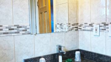 A bathroom with a marble-tiled wall, a sink with a black countertop, and a mirror above the sink.