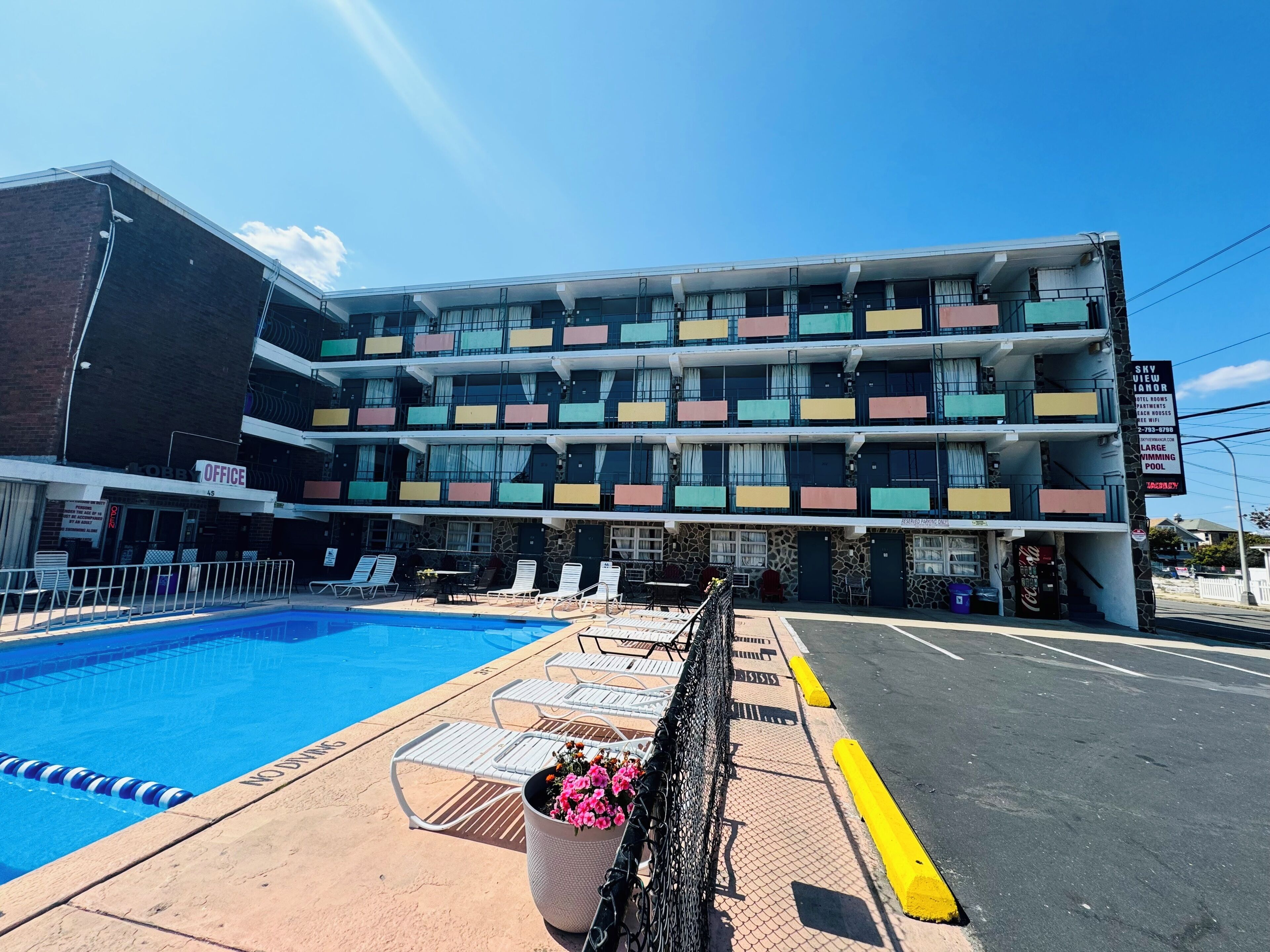 Ein mehrstöckiges Hotel mit Swimmingpool, Außenbereich zum Sitzen und einem Schild, das einen großen Swimmingpool bewirbt.