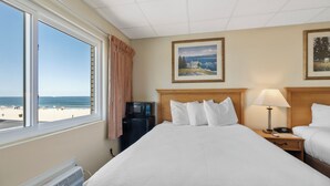 Una habitación de hotel con una cama grande, una mesita de noche con lámpara, un microondas y vista a la playa.