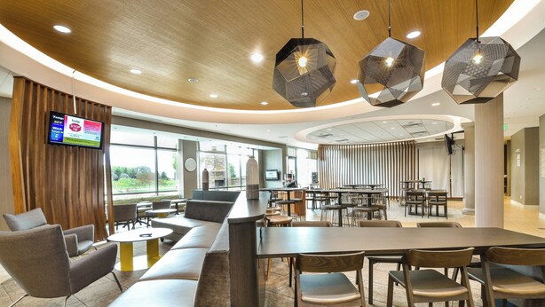 Un intérieur moderne avec un espace salon aux lignes courbes, une grande table et des suspensions lumineuses hexagonales.
