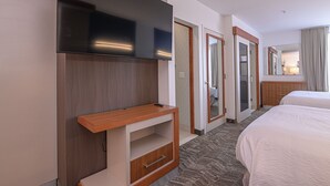 Une chambre d’hôtel dotée d’un téléviseur à écran plat fixé au mur, d’une console en bois, d’un lit avec une literie blanche, d’un sol recouvert de moquette et d’un miroir au-dessus du lit.