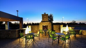 Un espace extérieur aménagé en terrasse, avec des murs en pierre, des chaises et des tables vertes, comprenant une cheminée en pierre et un coin salon abrité.