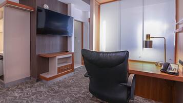 A hotel room with a desk, a chair, a flat-screen TV mounted on the wall, a telephone, and a sliding door.