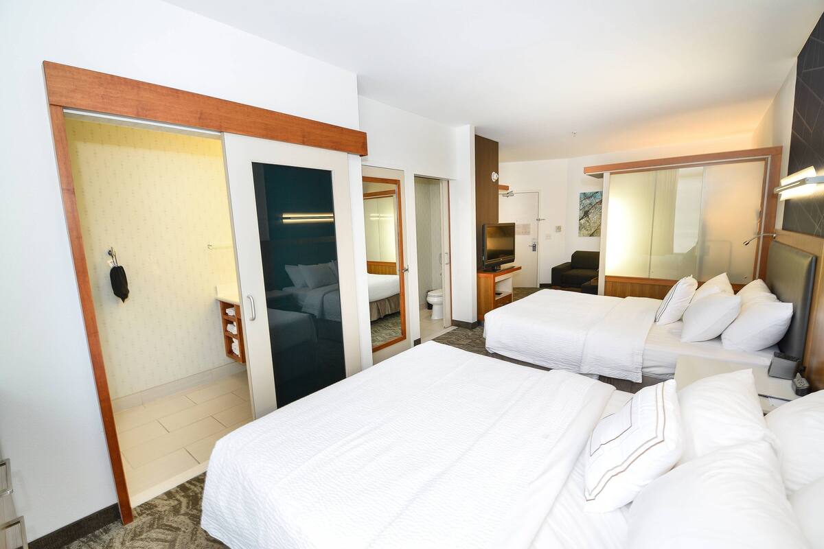 A hotel room with two beds, a TV, a desk, and a bathroom.