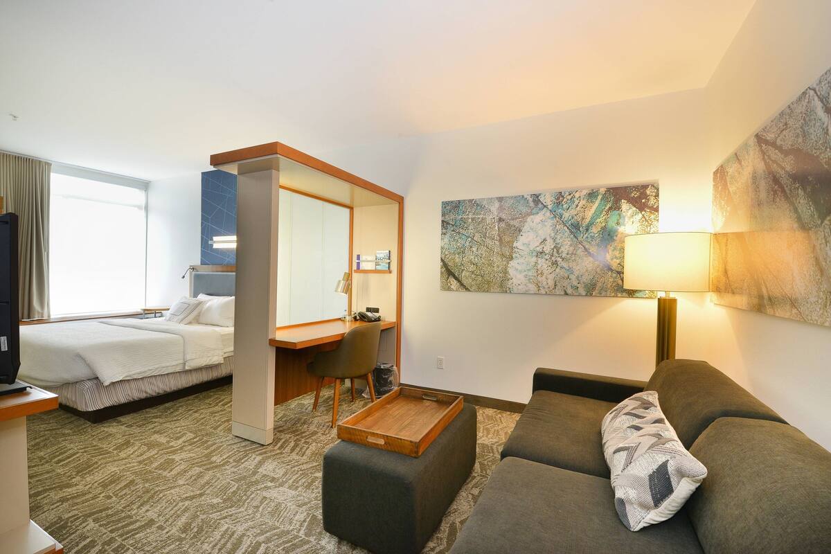 A hotel room with a bed, a desk, a chair, a sofa, and a painting on the wall.