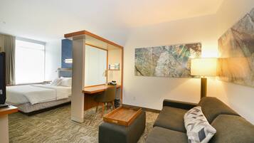 A hotel room with a bed, a desk, a chair, a sofa, and a painting on the wall.