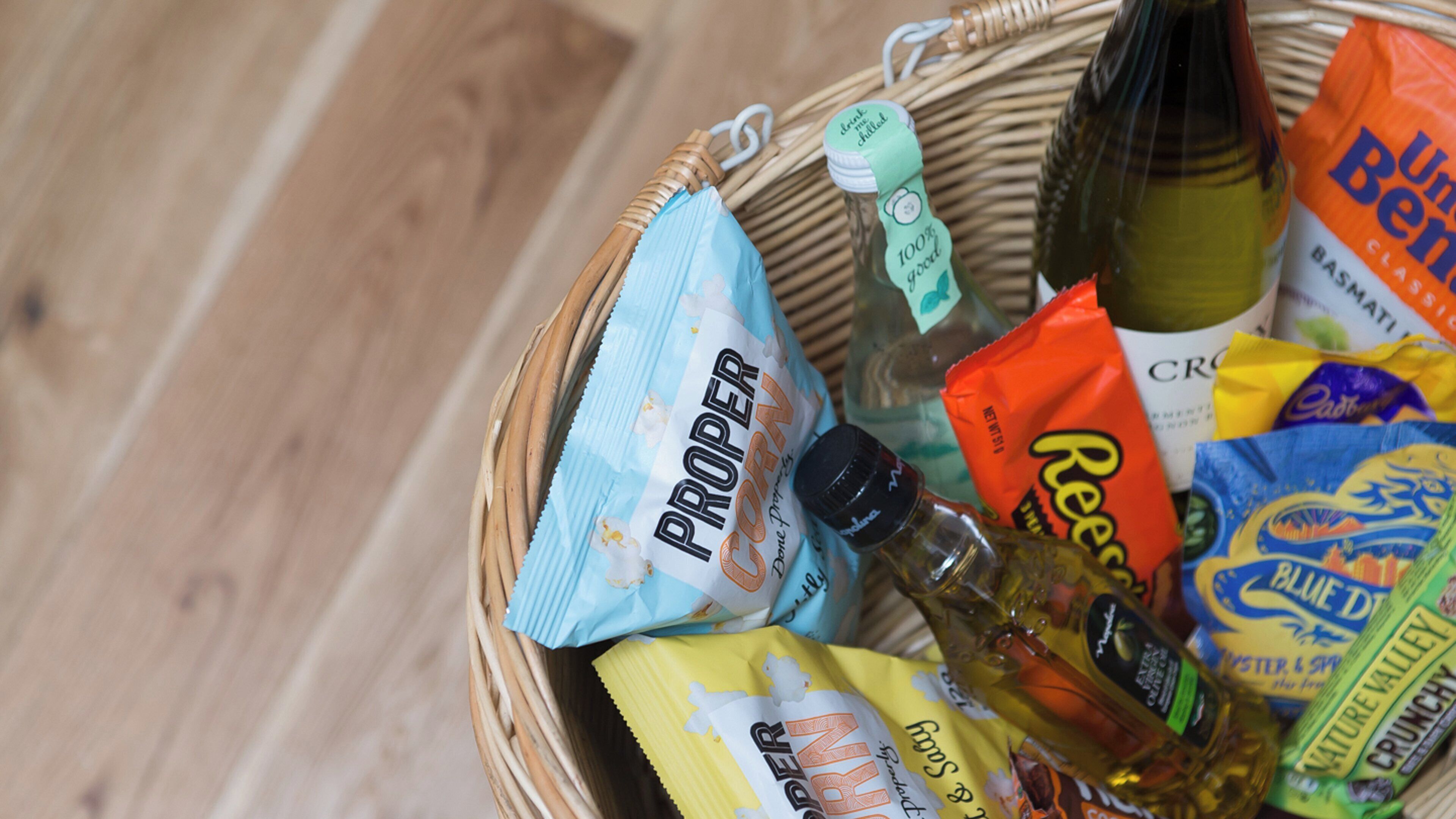 Ein Korbkistchen mit verschiedenen Lebensmitteln, darunter Snacks und eine Flasche Öl.