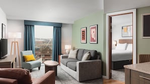 A modern hotel room with a grey sofa, a small round table, a blue armchair, a bed with white bedding, and artwork on the walls. - Staybridge Suites Newcastle by IHG (Newcastle-upon-Tyne)