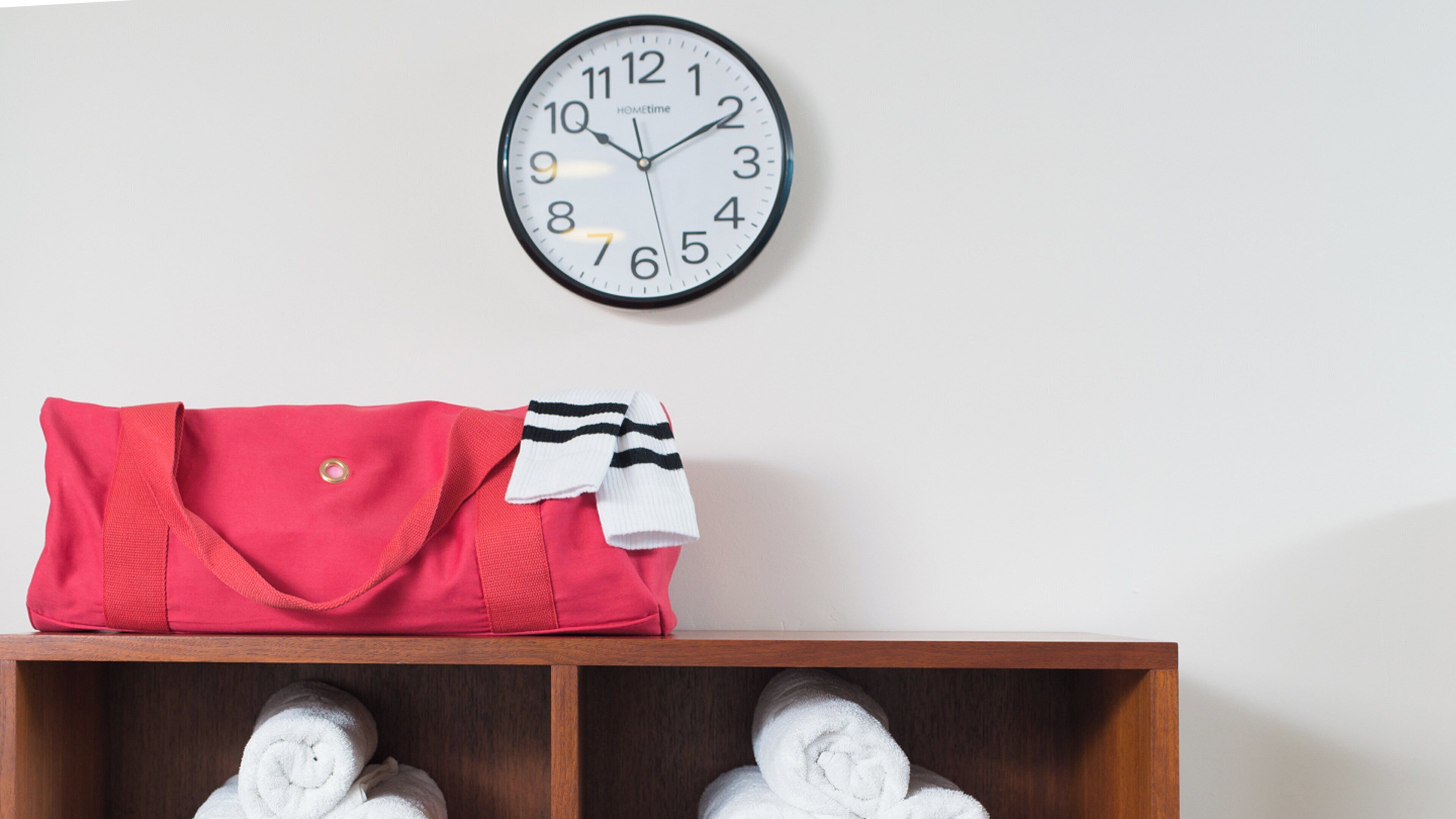 Une horloge murale, un sac rouge et une étagère avec des serviettes pliées.