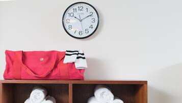 Une horloge murale, un sac rouge et une étagère avec des serviettes pliées.