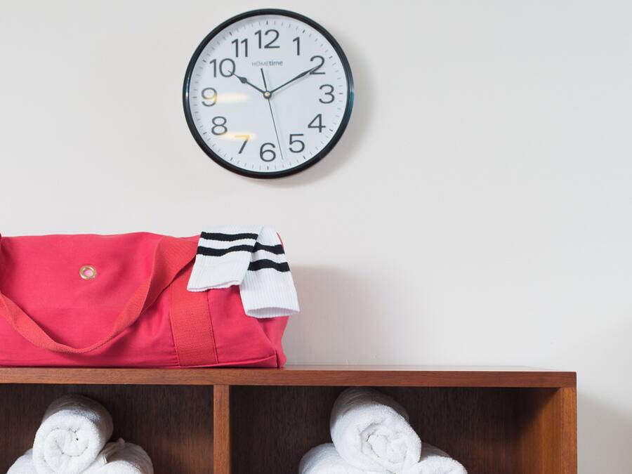 Une horloge murale, un sac rouge et une étagère avec des serviettes pliées.