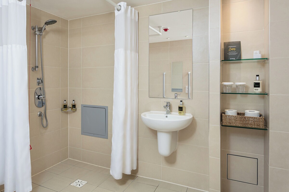 A modern bathroom with a shower, sink, and shelves with toiletries.