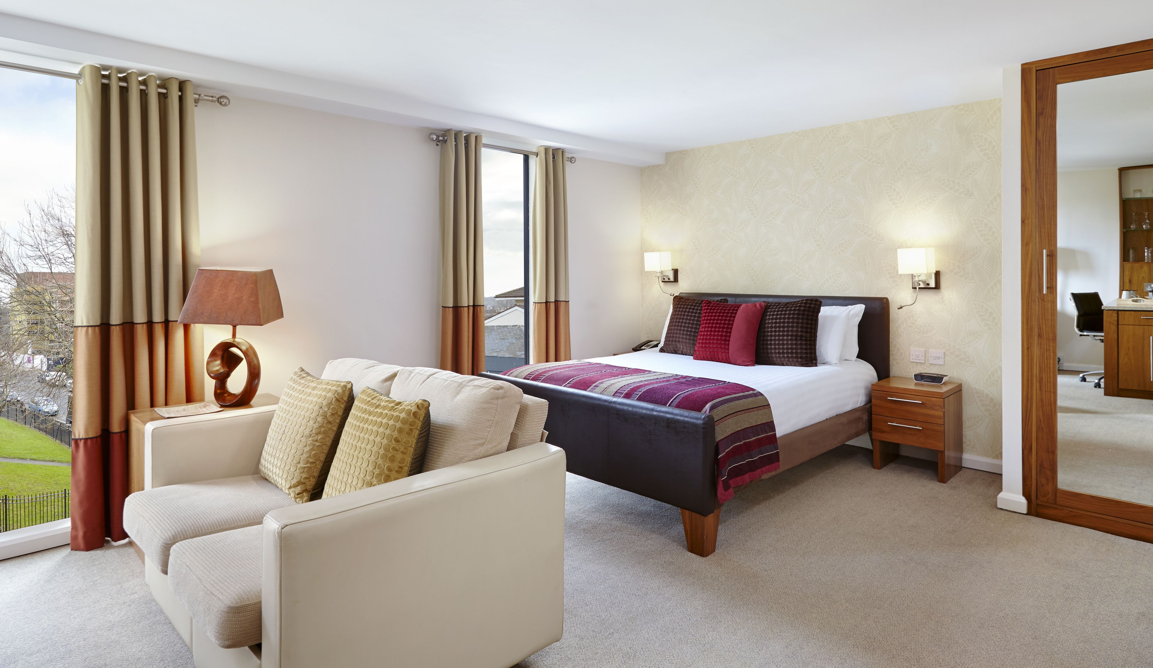 A hotel room with a bed, bedside table, lamp, and a chair.