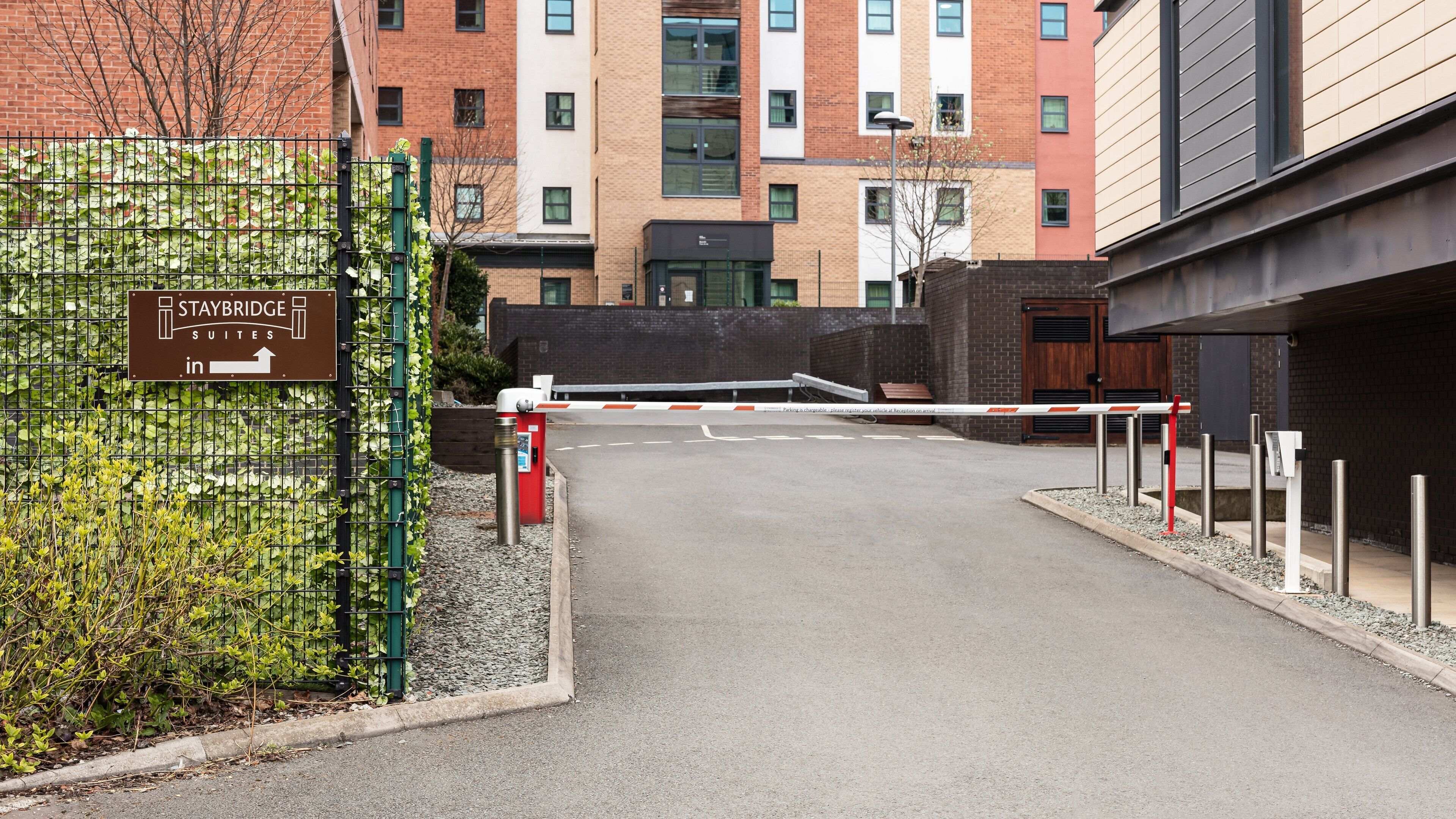 A gated entrance to Staybridge Suites with a sign, a metal barrier, and a building in the background.