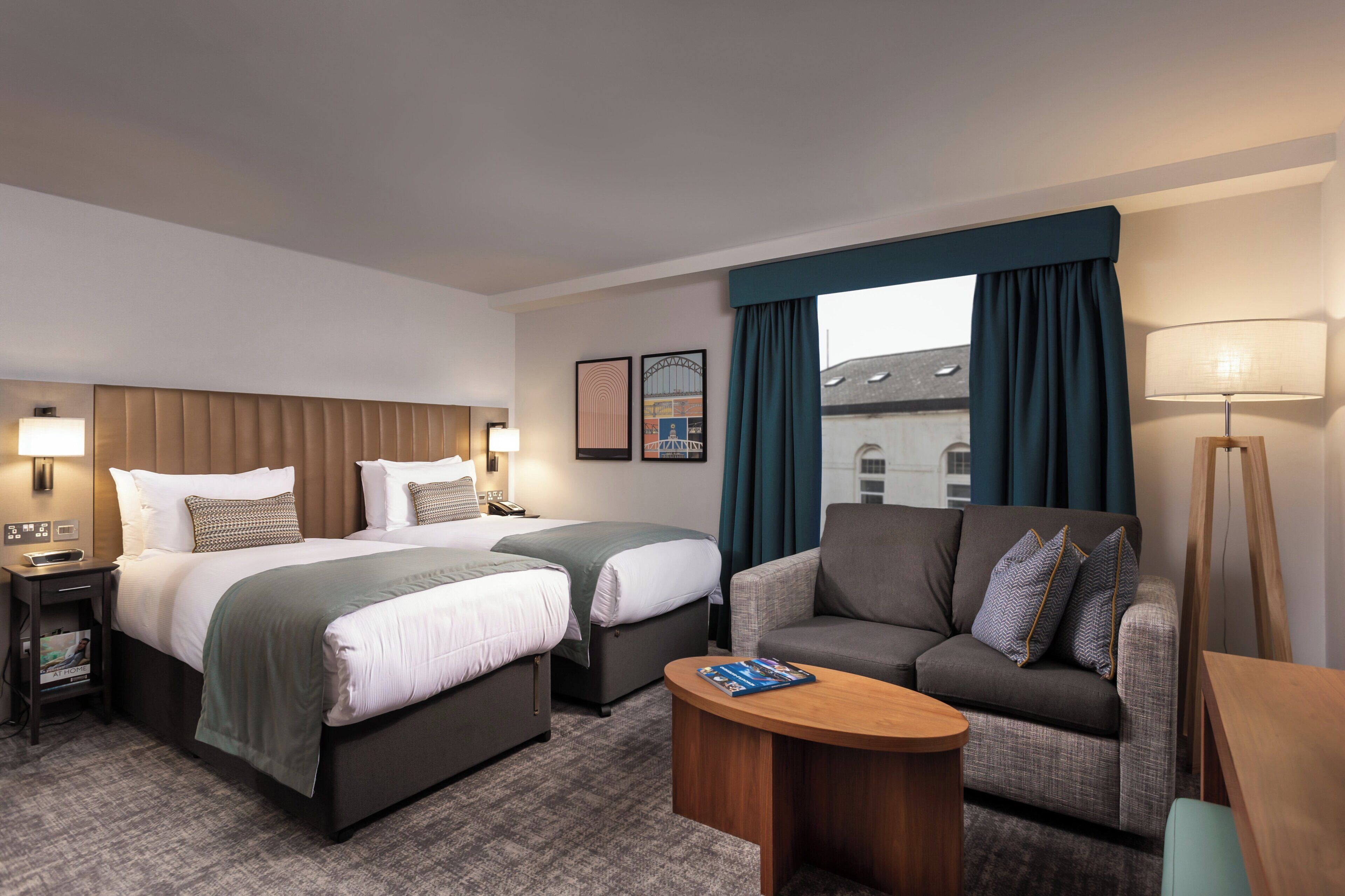 A hotel room with two beds, a sofa, a coffee table, and a lamp.