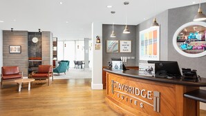 A reception area with a wooden reception desk, seating area with chairs, and a modern interior design. - Staybridge Suites Newcastle by IHG (Newcastle-upon-Tyne)