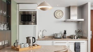 A modern kitchen with a stainless steel microwave, a coffee machine, and a toaster. There is a clock on the wall and a wooden tray with cups and a coffee pot. - Staybridge Suites Newcastle by IHG (Newcastle-upon-Tyne)
