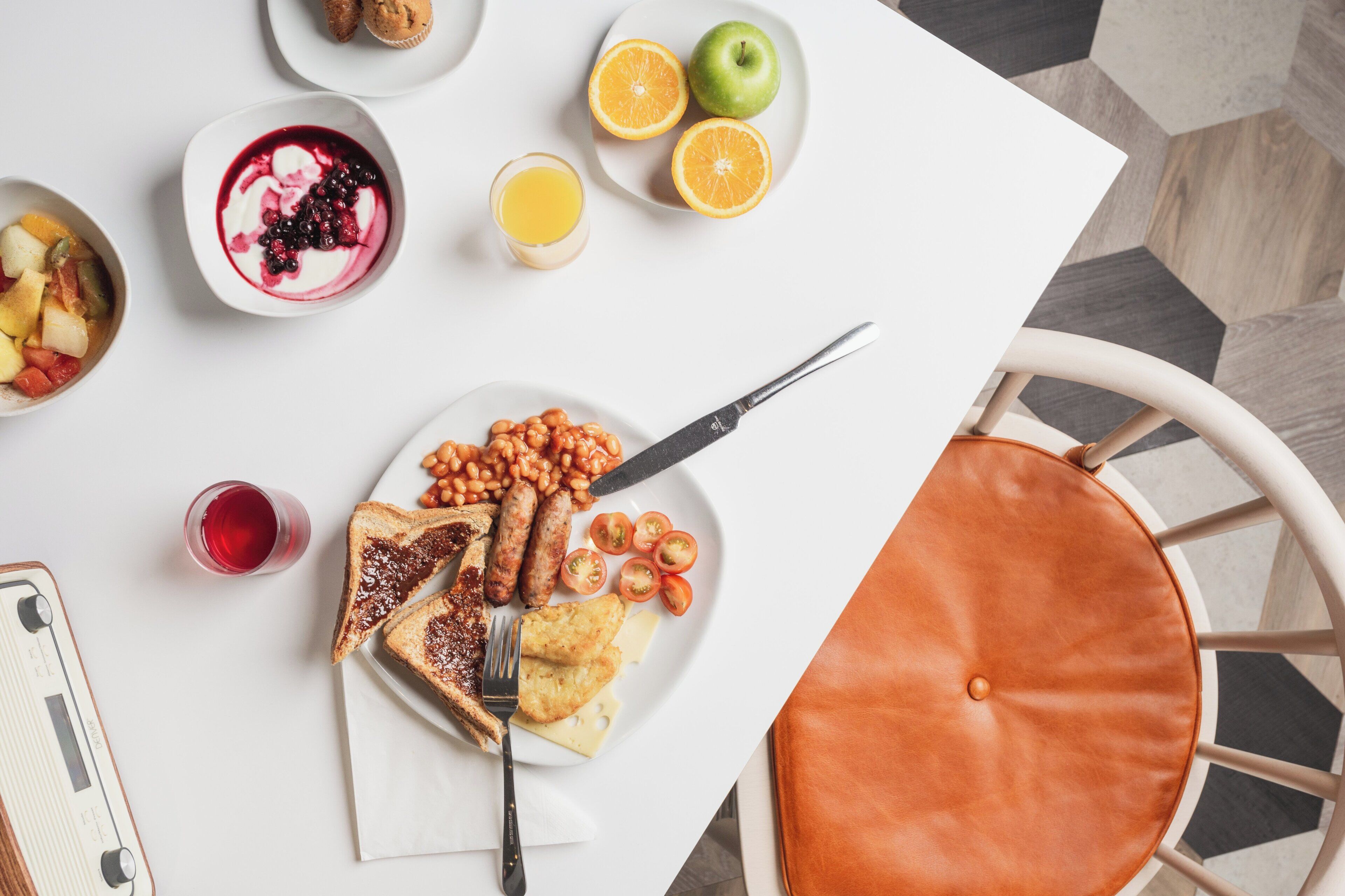 A breakfast table with toast, beans, sausages, tomatoes, and a glass of juice.