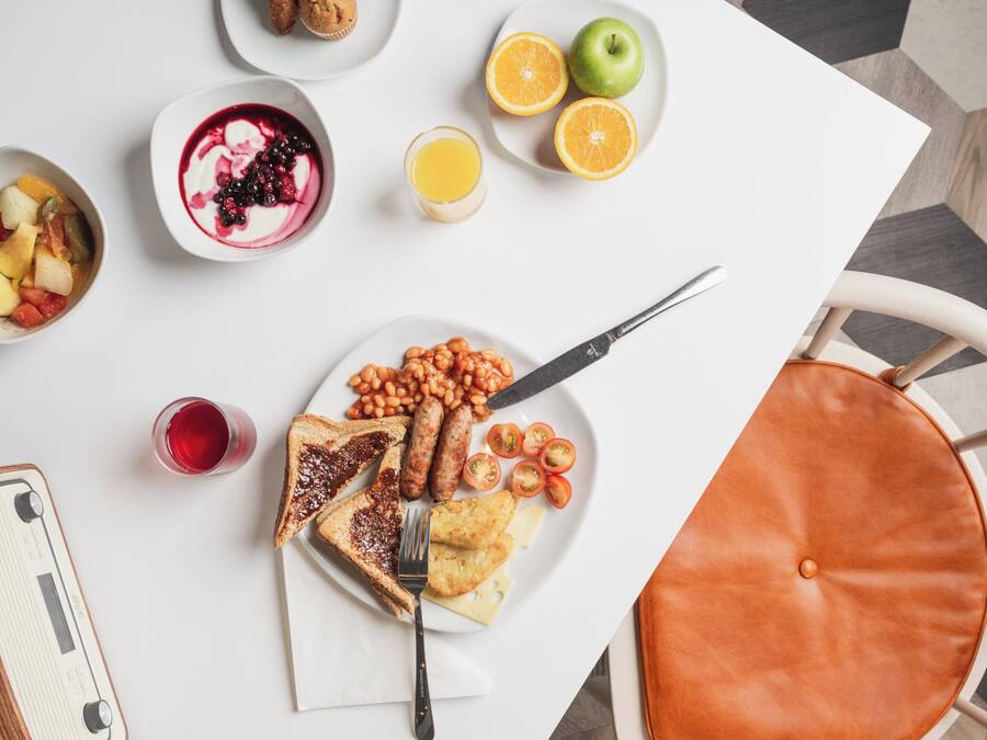 A breakfast table with toast, beans, sausages, tomatoes, and a glass of juice.