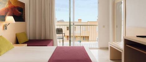 Habitación de hotel con cama, escritorio, silla, balcón y vista a edificios, además de un cuadro en la pared.