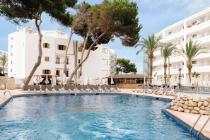 A swimming pool with lounge chairs and umbrellas, surrounded by white buildings and trees. - Bluesea Coral Beach (Santa Eulalia del Rio)