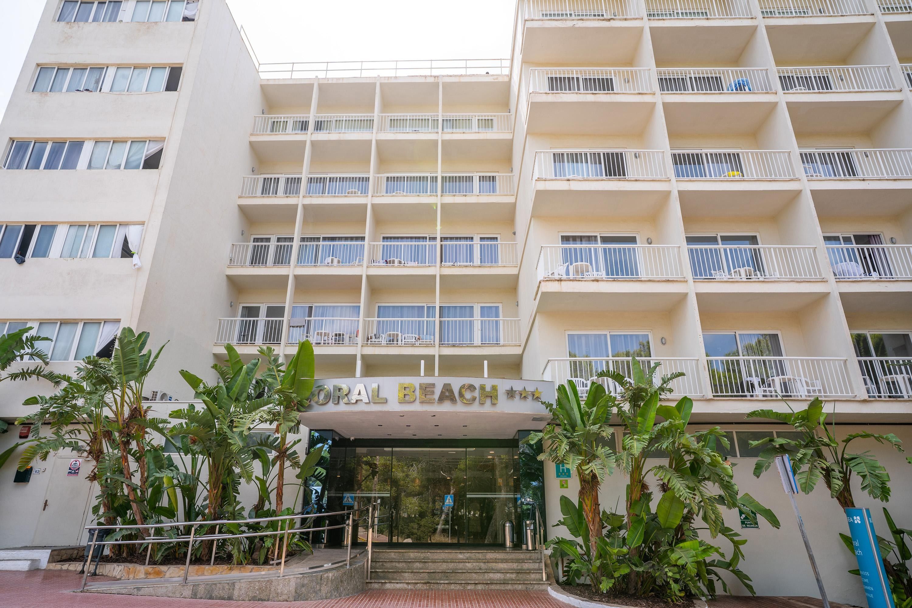 Un hotel de varios pisos con balcones, un cartel que dice 'Oral Beach' y una escalera que lleva a la entrada.
