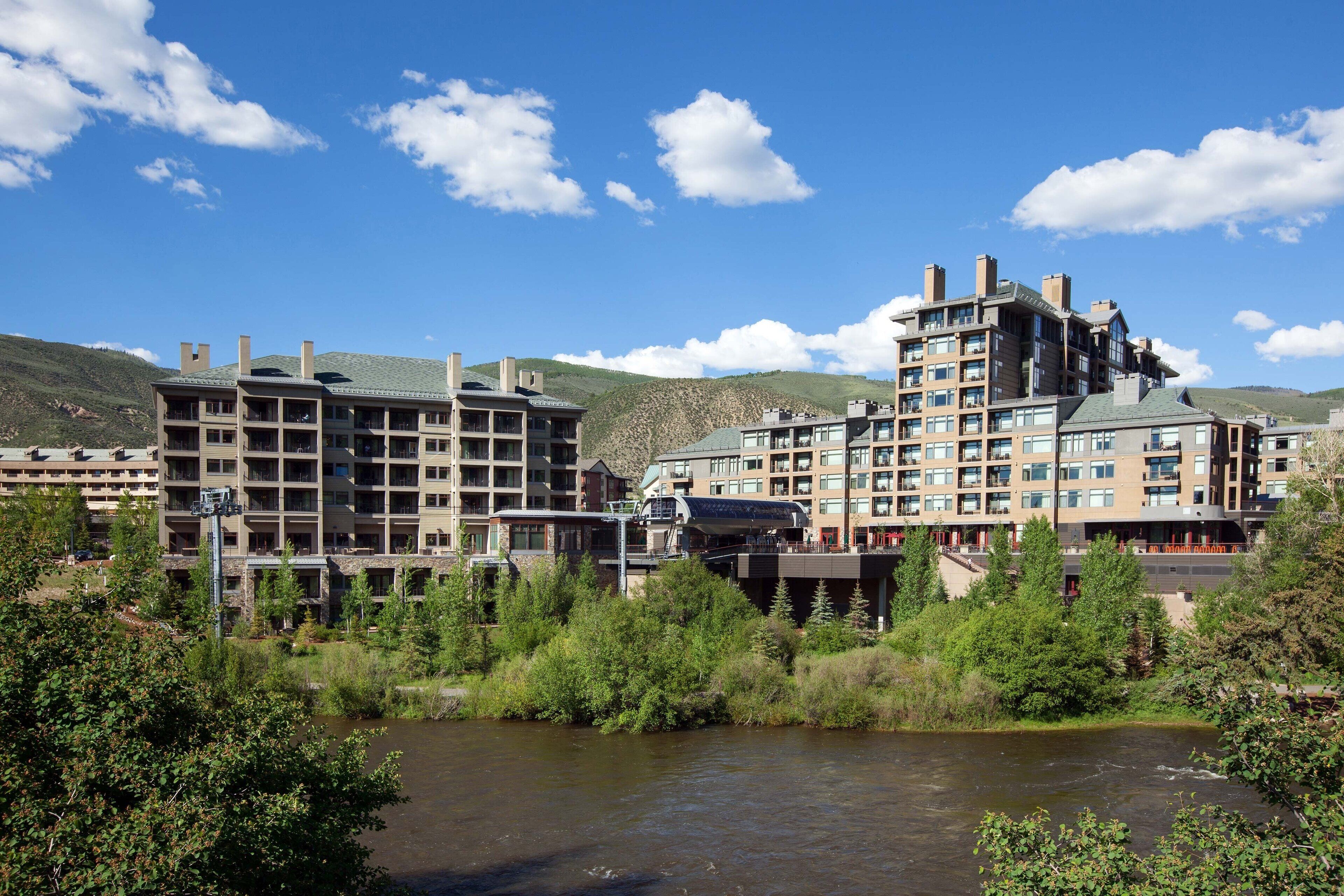A multi-story hotel with a modern architectural design, situated near a river with lush greenery.