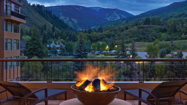 Un balcon doté d’un foyer, offrant une vue sur un paysage montagneux, avec des arbres et des bâtiments en arrière-plan.