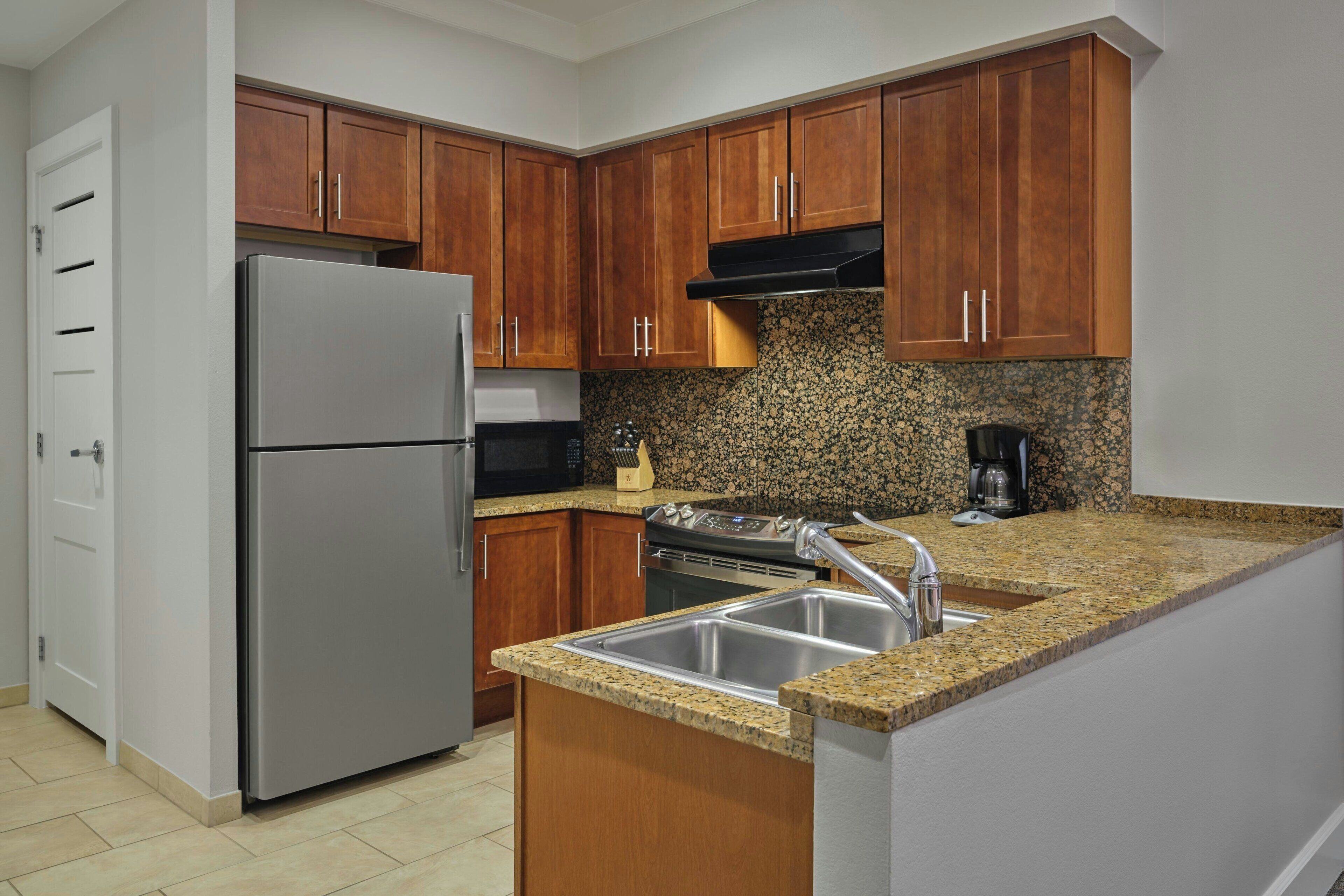 A kitchen with wooden cabinets, a stainless steel refrigerator, a granite countertop, and a built-in sink.