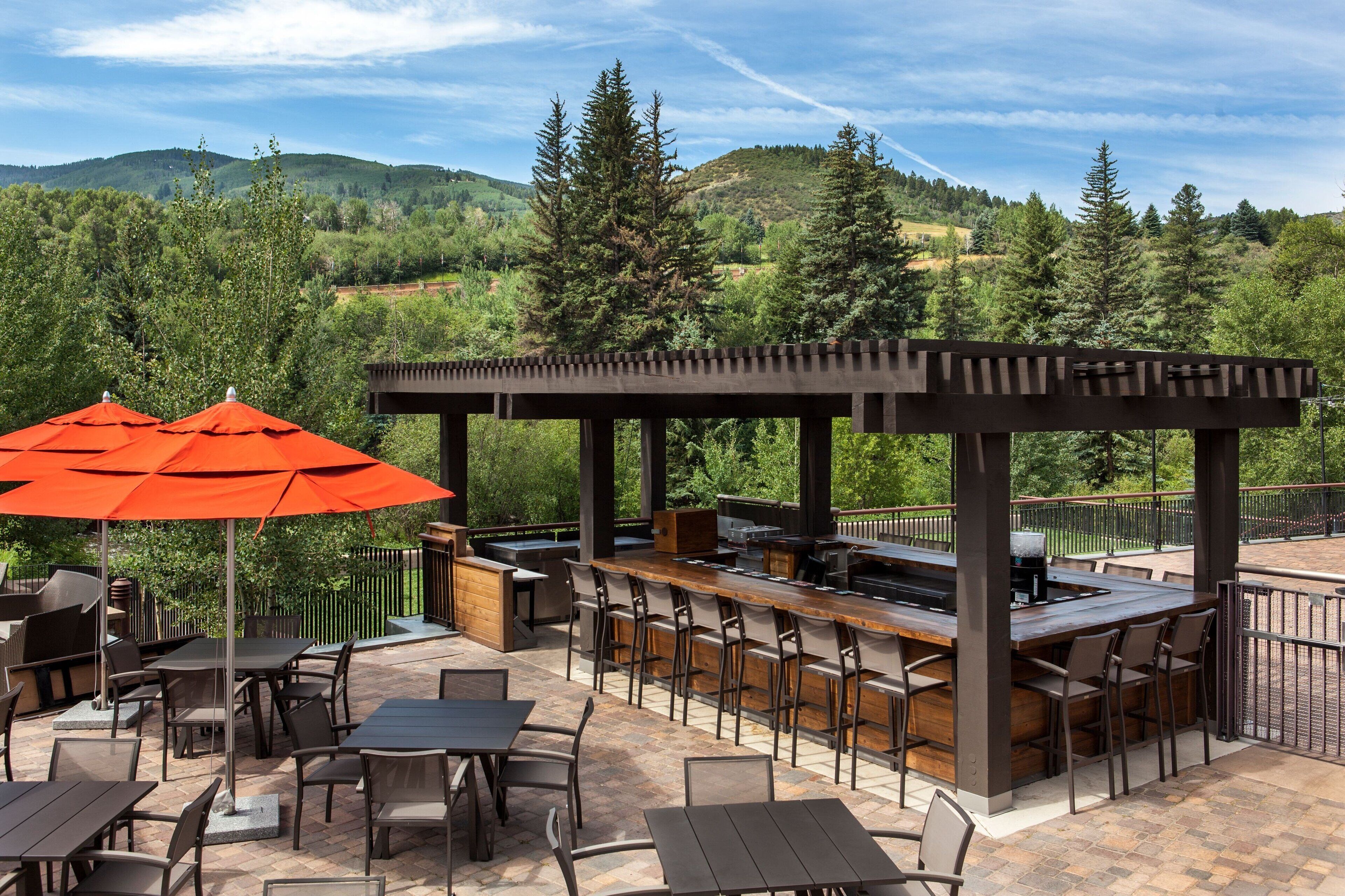An outdoor patio with a bar area, seating, and a pergola with umbrellas.