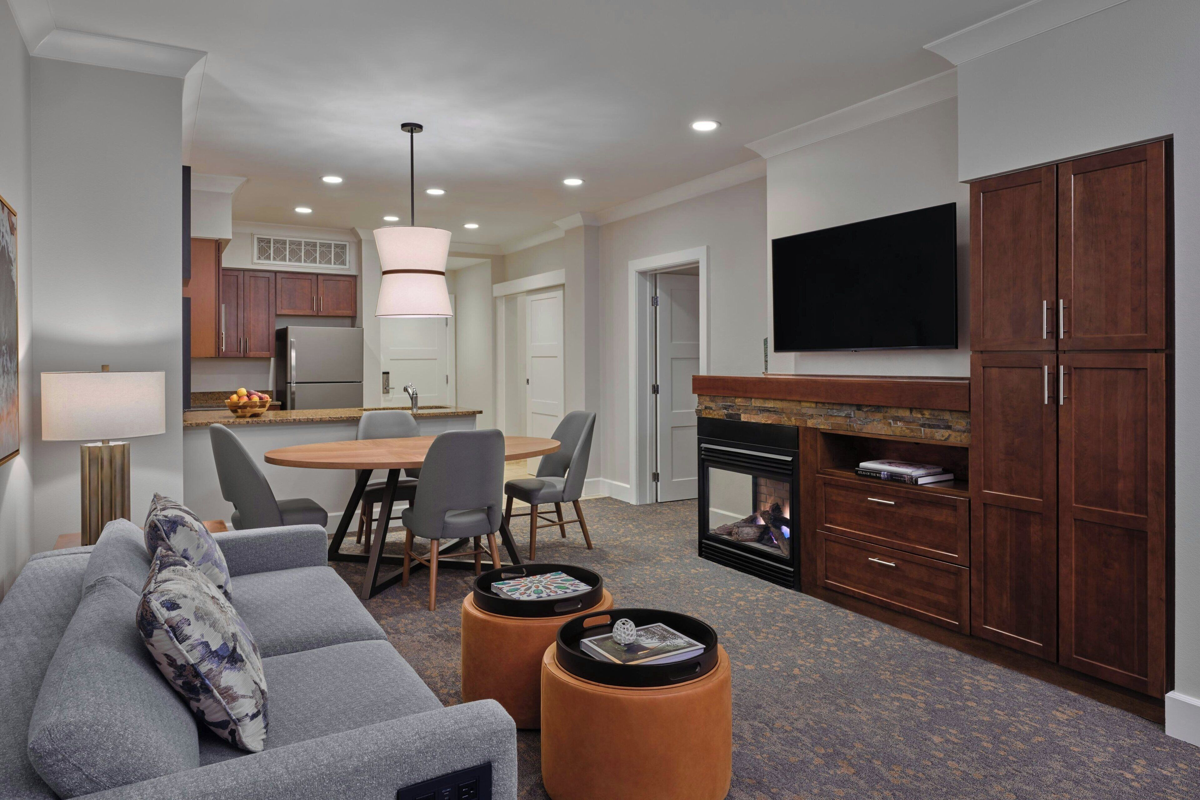 A modern living room with a gray sofa, ottomans, a fireplace, and a dining area with chairs and a table.