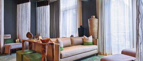 A modern hotel room with a sofa, ottomans, a wooden side table, and a large vase.