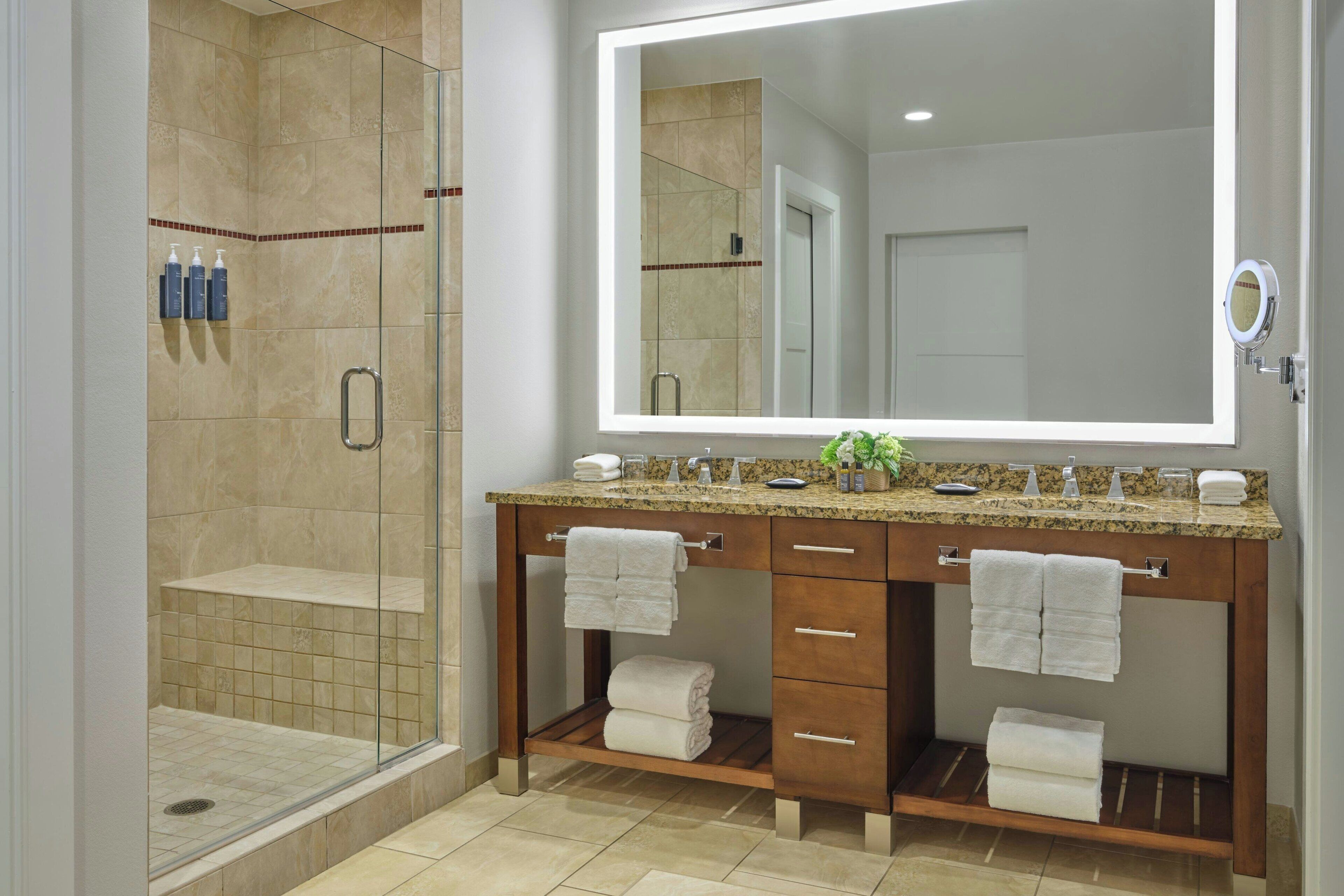 A bathroom with a glass-enclosed shower, a large mirror, and a vanity with two sinks and towel racks.