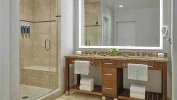 A bathroom with a glass-enclosed shower, a large mirror, and a vanity with two sinks and towel racks.