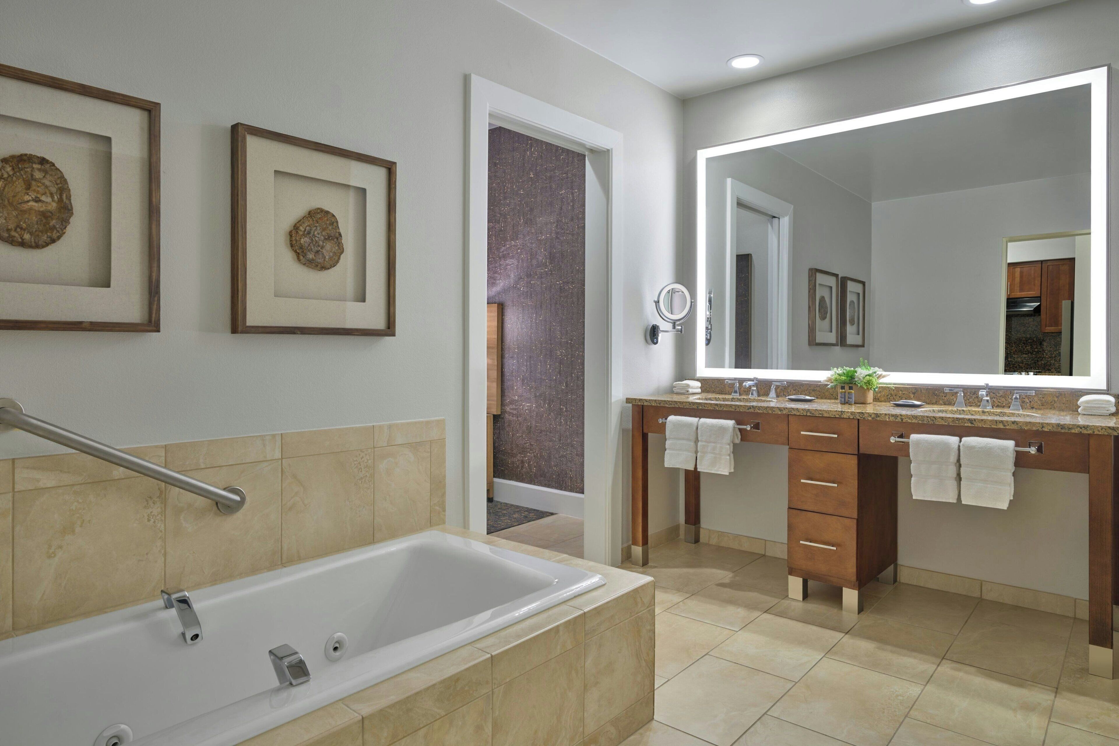 Un bagno moderno con vasca, doppio lavabo con specchio, opere d'arte incorniciate e zona doccia a vista.