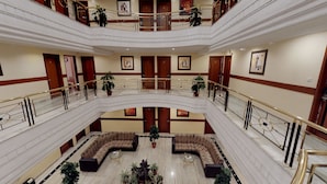 Um hall de hotel amplo em vários níveis, com pisos de mármore, área de estar central com sofás e uma varanda com grades.