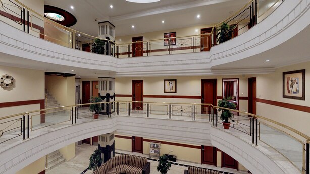 Um hall de hotel em vários níveis, com piso de mármore, uma escadaria central e várias portas.