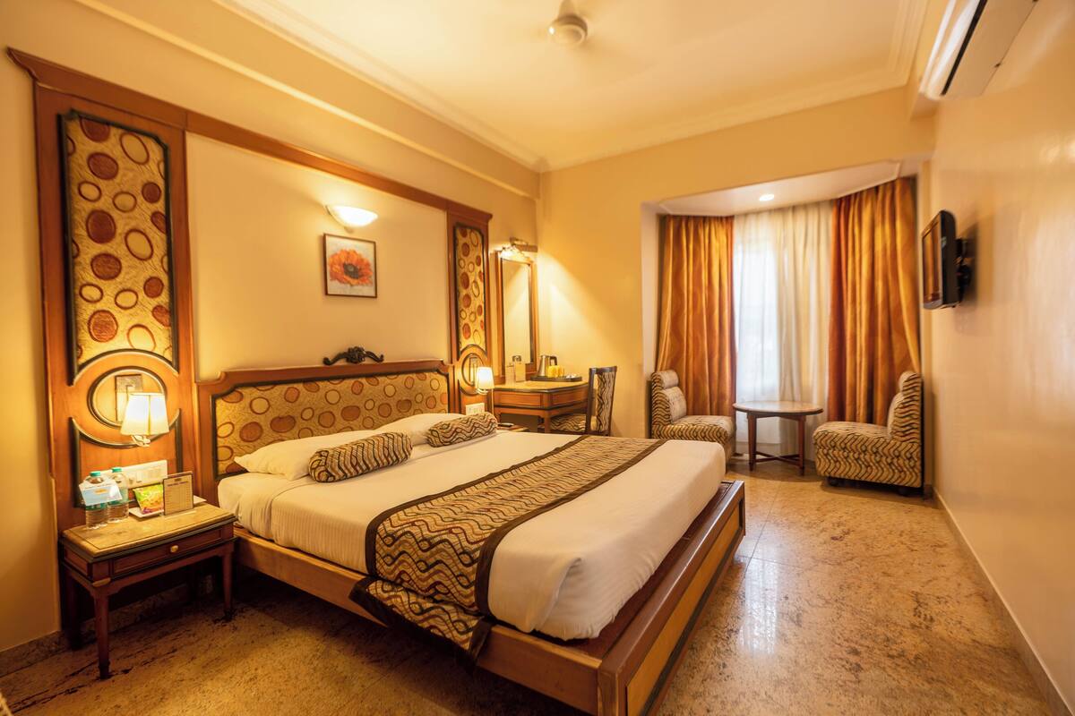 A hotel room with a large bed, a desk, a chair, and a small table.