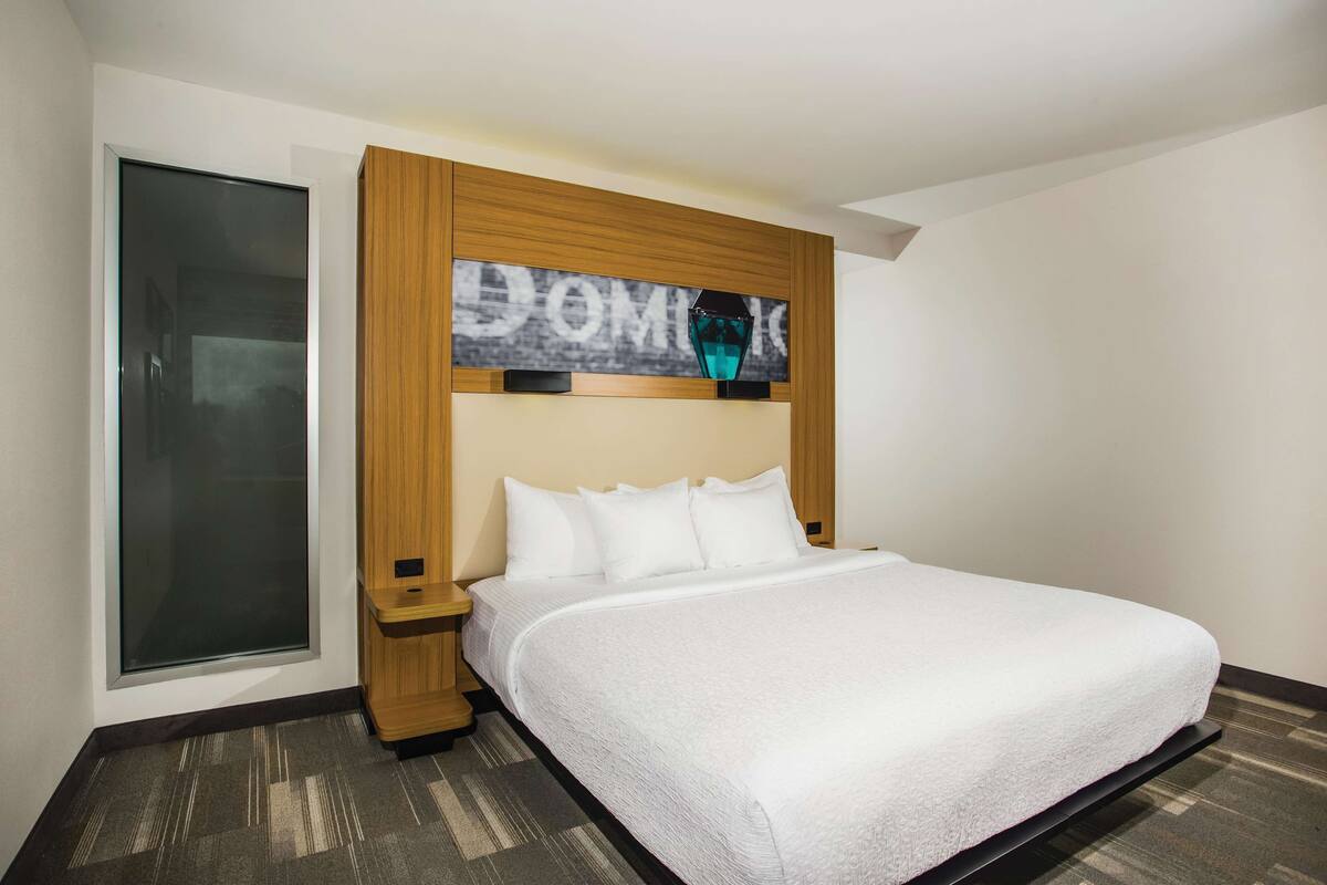 Une chambre d’hôtel avec un grand lit, une tête de lit en bois, une table de chevet et une grande fenêtre.