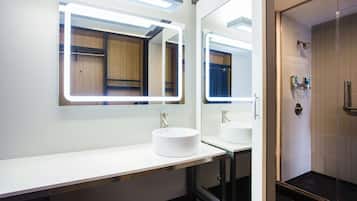 A modern bathroom with a large mirror, two sinks, and a shower area.