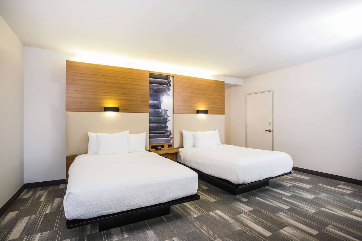 Une chambre d’hôtel avec deux lits, une tête de lit en bois, une grande œuvre d’art accrochée au mur et un sol recouvert de moquette.