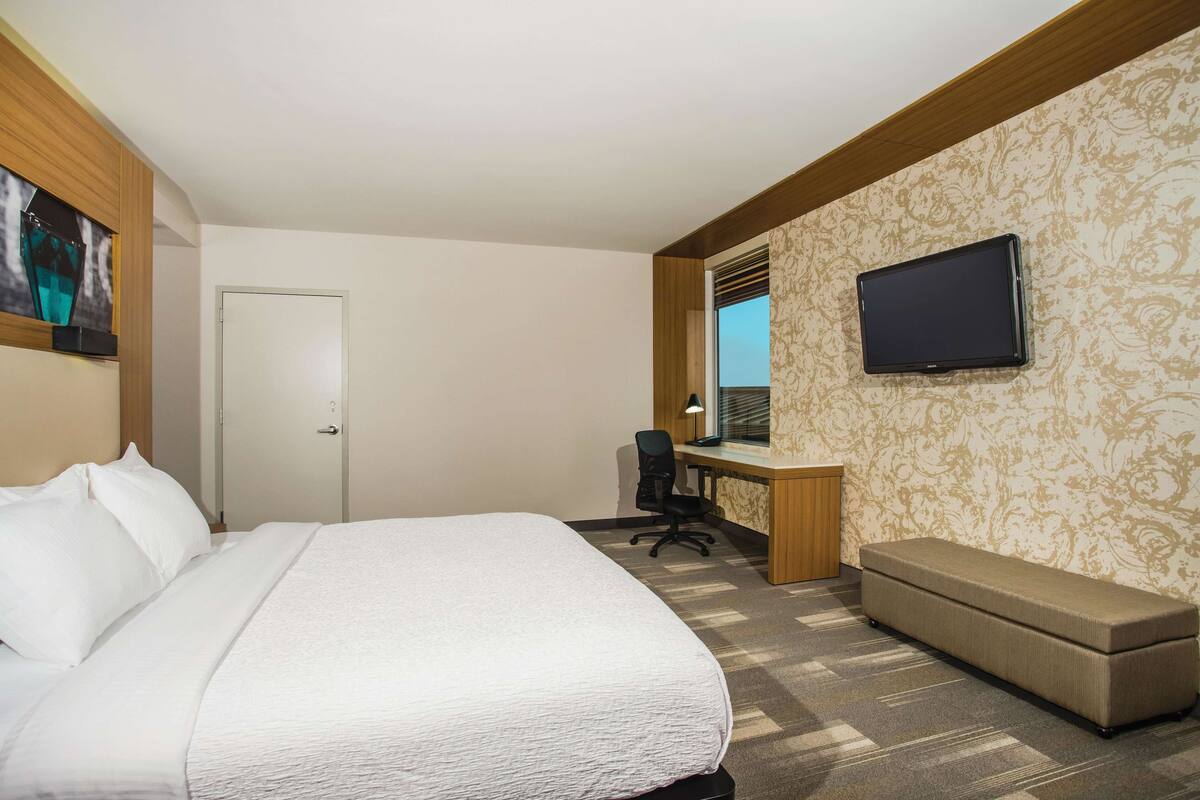 Une chambre d’hôtel avec un lit, un bureau avec un ordinateur, une télévision et un banc.