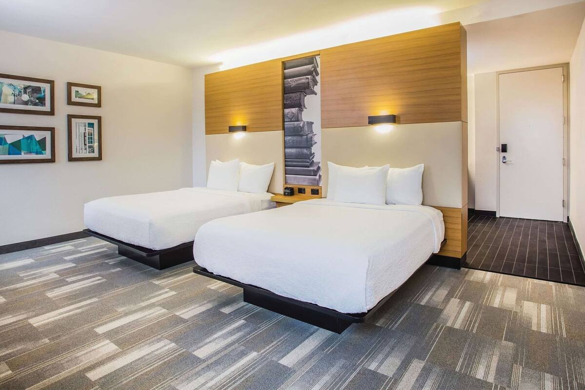 Une chambre d’hôtel avec deux lits, une tête de lit en bois, des lampes fixées au mur et une porte.